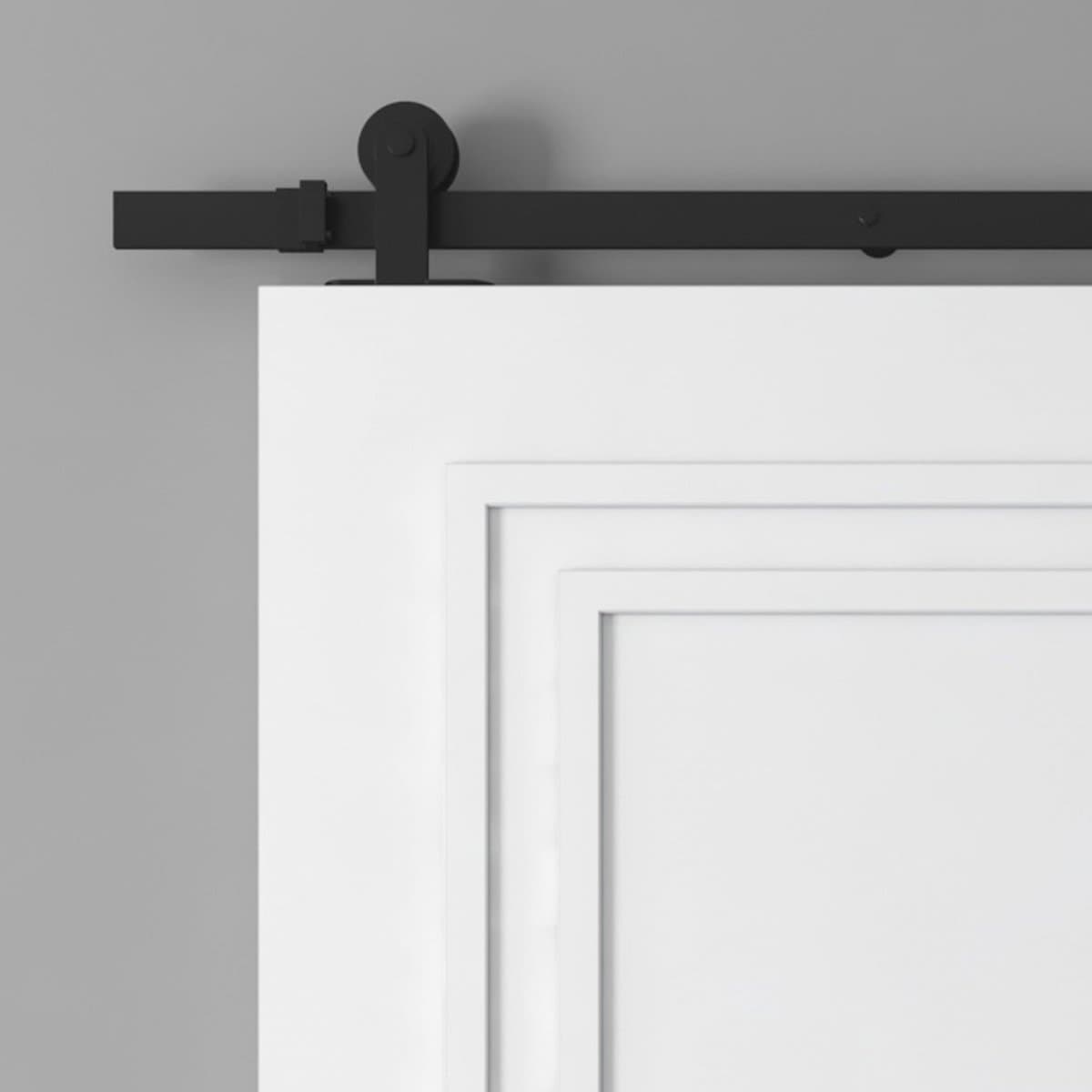 A close-up of the upper section of a white barn door with a black sliding hardware track mounted on a grey wall.