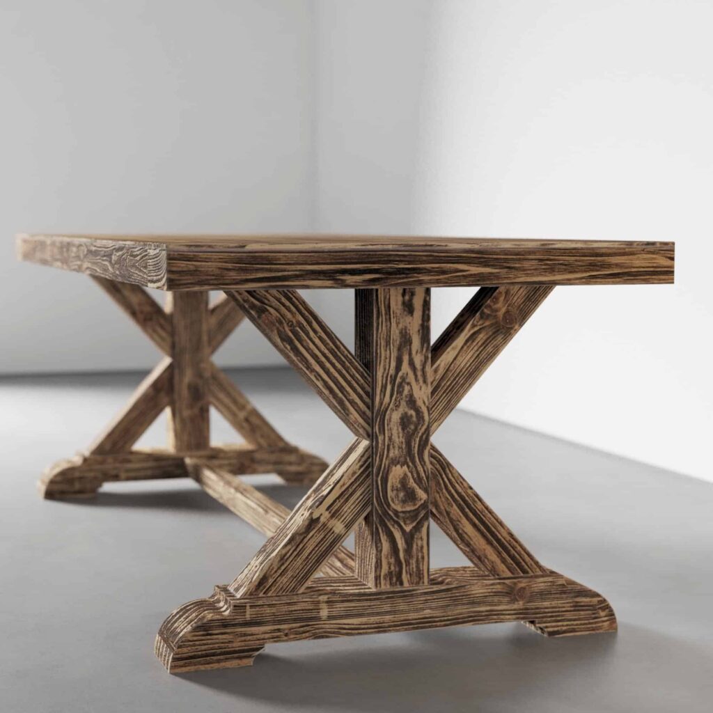 A rustic wooden table with an X-shaped support structure shown from an angle. The table has a weathered finish and sits on a gray floor against a light-colored wall.