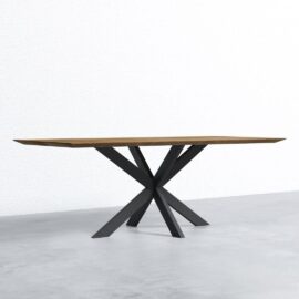 A rectangular wooden table with a modern, black, geometrically designed metal base stands on a concrete floor against a white textured wall.