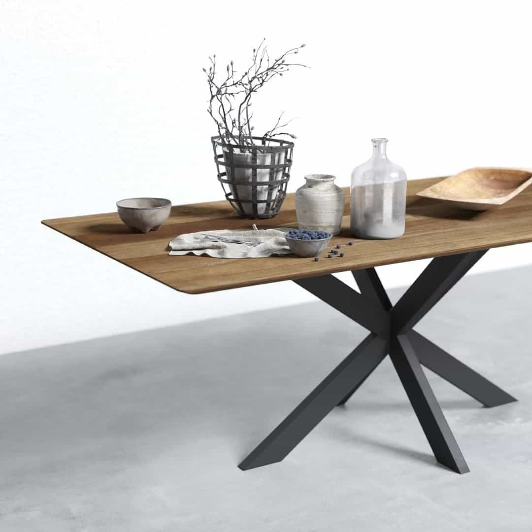 A modern wooden table with black metal legs, holding various ceramic and glassware, including bowls, a vase with twigs, a cloth, a wooden tray, and scattered dark berries.