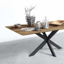 A modern wooden table with black metal legs, holding various ceramic and glassware, including bowls, a vase with twigs, a cloth, a wooden tray, and scattered dark berries.