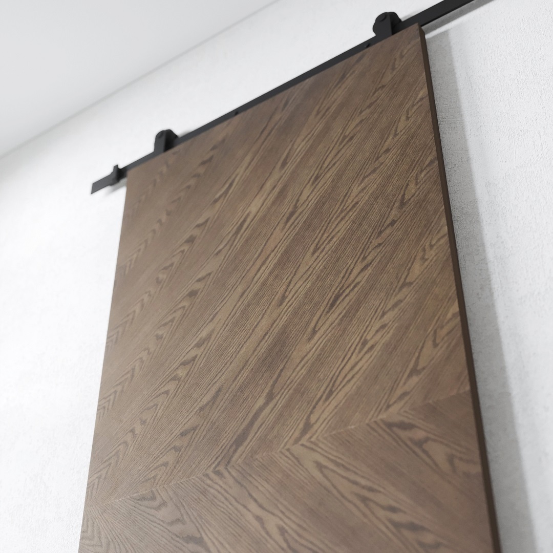 BIANCO - DARK 2 A close-up view of the Bianco Barn Door, featuring a chevron pattern and mounted on a black metal track against a white wall.