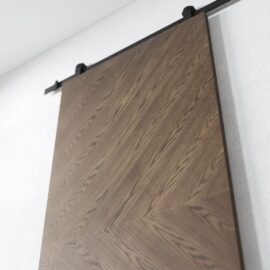 A close-up view of the Bianco Barn Door, featuring a chevron pattern and mounted on a black metal track against a white wall.