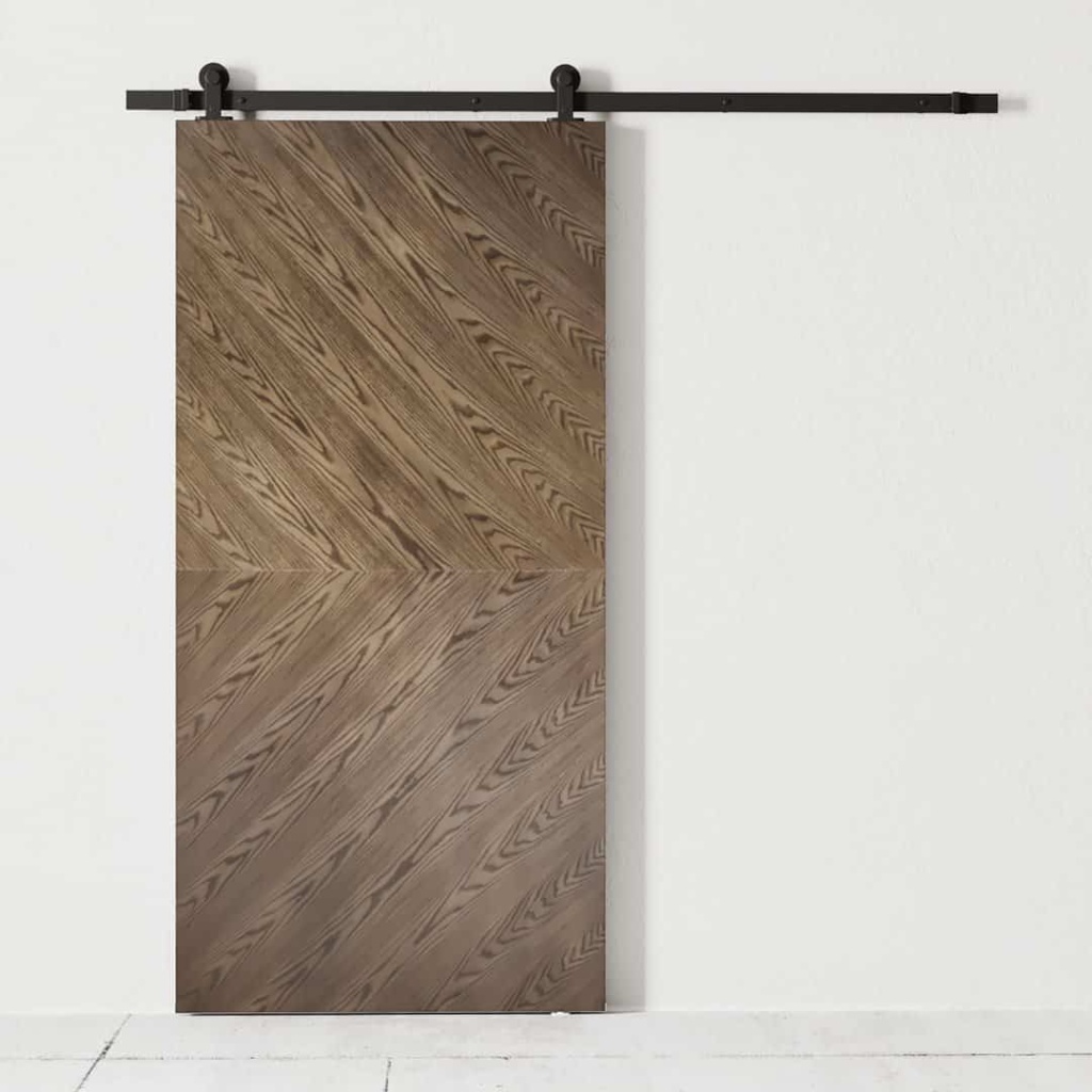 A wooden sliding barn door with a chevron pattern, mounted on a black metal track, stands elegantly against the bianco white wall.