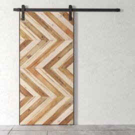 The Chevron 83" x 40" Barn Door, featuring a sliding design made from wooden slats in varying shades arranged in a chevron pattern, is mounted on a black metal track against a plain, light-colored wall.