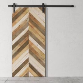 The Herringbone 83" x 40" Barn Door, featuring a chevron wood pattern in various shades of brown and beige, is mounted on a white textured wall.