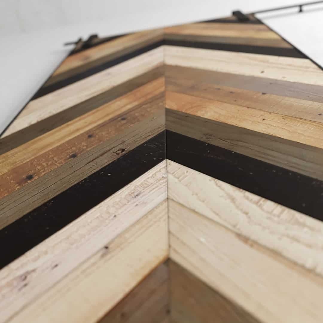Close-up of a Herringbone 83" x 40" Barn Door featuring a wooden surface with a chevron pattern made of alternating light and dark wood strips.