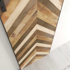 A close-up of the Herringbone 83" x 40" Barn Door showcases its distinct chevron pattern, featuring alternating light and dark wooden planks. The barn door is mounted vertically against a white wall.