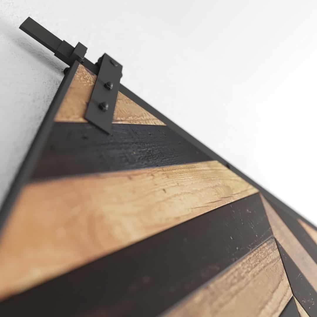 Close-up of the Herringbone 83" x 40" Barn Door, showcasing a diagonal pattern of alternating light and dark wood panels framed in metal. The metal slider mechanism is visible at the top of the door.