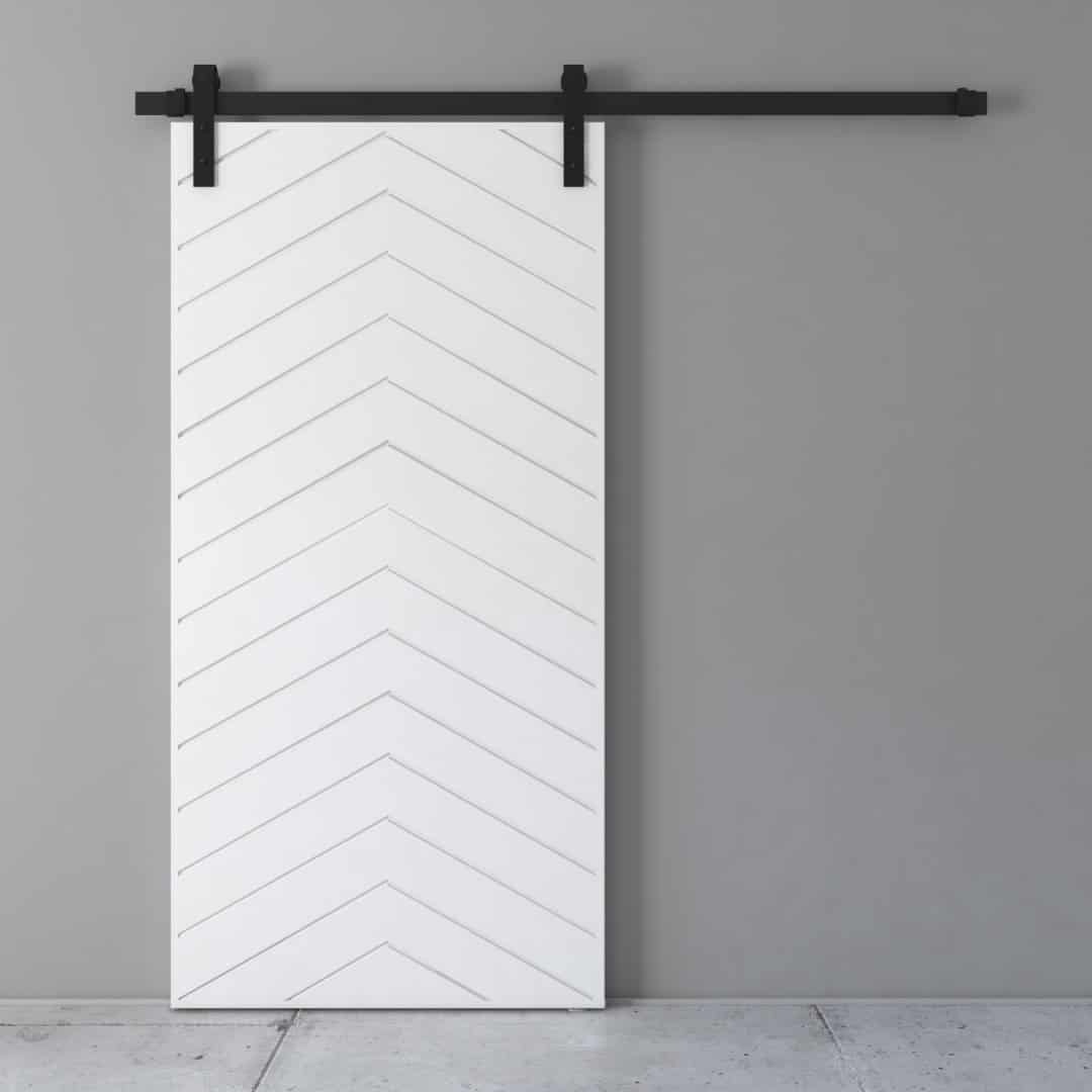 A white Osaka Barn Door with a chevron pattern is mounted on a black sliding track against a gray wall.