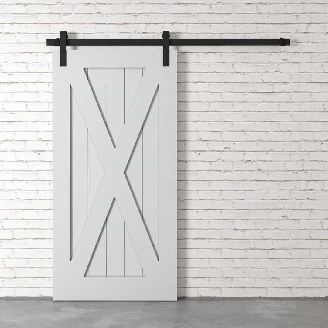 The X-Panel Barn Door, featuring a white barn-style design with black hardware, is installed on a white brick wall.