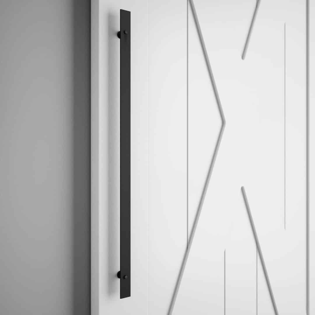 An 18th Street Barn Door Handle in black is mounted vertically on a white door with geometric patterns, which is partially visible against a plain wall.