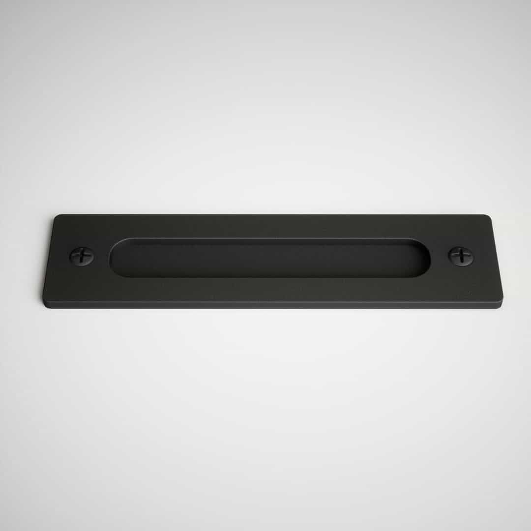 A black barn door handle with a rectangular shape and two screws on either end, mounted on a flat, light-colored surface.