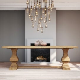 A Castello Dining Table - Natural with ornate legs is placed in front of a fireplace with a modern design, under a chandelier featuring multiple hanging light bulbs.