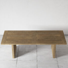 The Camden Dining Table, featuring a light brown finish and a wooden rectangular design, stands on a light gray tiled floor against a plain white wall.