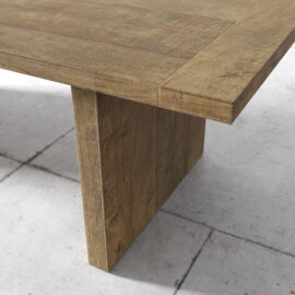 Close-up view of the Camden Dining Table with a thick, sturdy leg set on a tiled floor. The table has a natural wood finish with visible grain patterns.