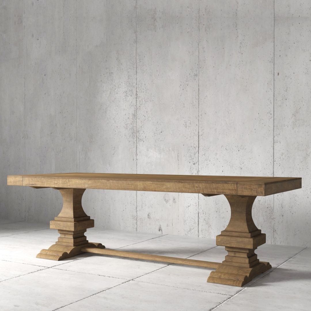 Castello Dining Table 2 The Castello Dining Table - Natural features a wooden rectangular top with two ornate pedestal legs, set on a concrete floor against a gray wall.