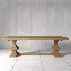 A Castello Dining Table in a natural wood finish featuring two pedestal legs, set on a white tiled floor against a gray concrete wall.