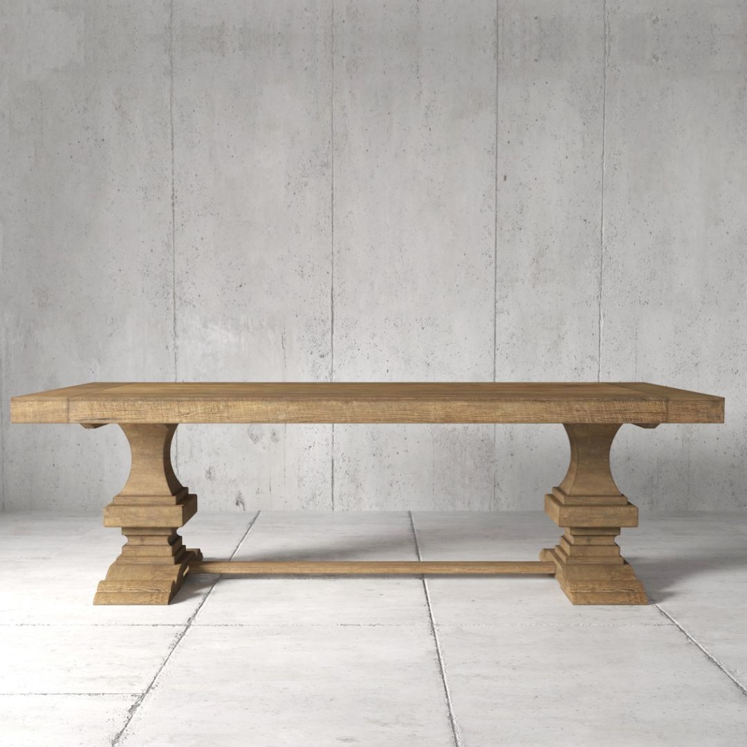 A Castello Dining Table in a natural wood finish featuring two pedestal legs, set on a white tiled floor against a gray concrete wall.