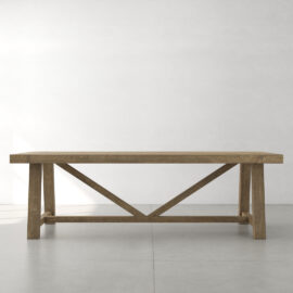 A Farmhouse Dining Table featuring a rectangular wooden top and X-frame support underneath, placed in a minimalistic room with a light-colored floor and wall.