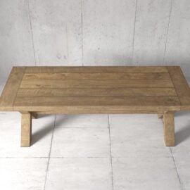 The Grand Cross Dining Table, a wooden rectangular piece with thick legs, stands on a tiled floor against a concrete wall background.