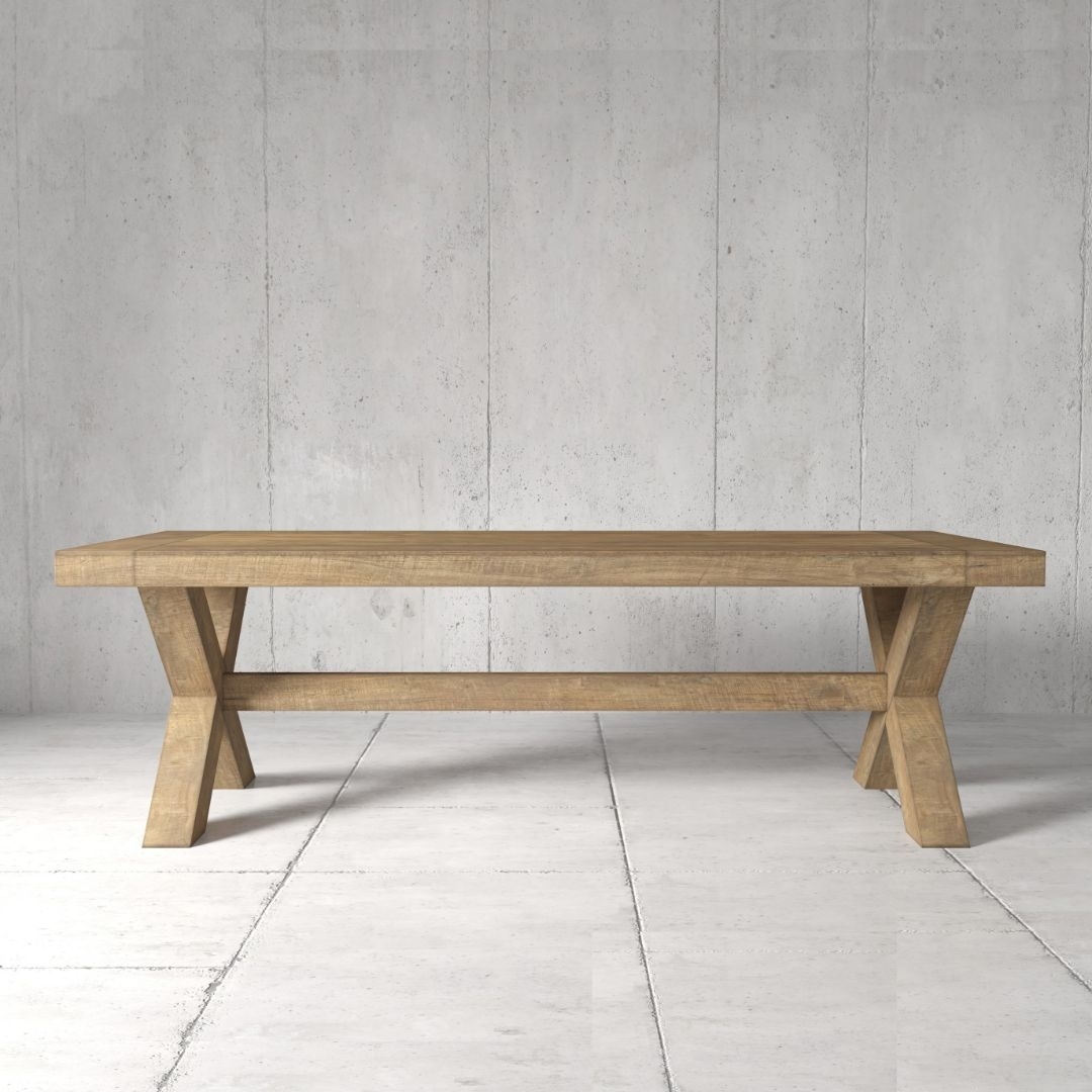The Grand Cross Dining Table, featuring its distinctive X-shaped legs, stands in a minimalistic, grey-tiled room with a plain concrete wall backdrop.