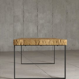 The Hudson Dining Table, featuring a wrinkled yellow fabric top and black metal legs, stands on a concrete floor against a concrete wall.
