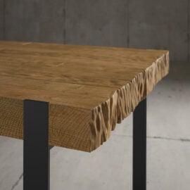 Close-up of the Hudson Dining Table with a carved, uneven edge. The table has a natural wood finish and is supported by black metal legs.