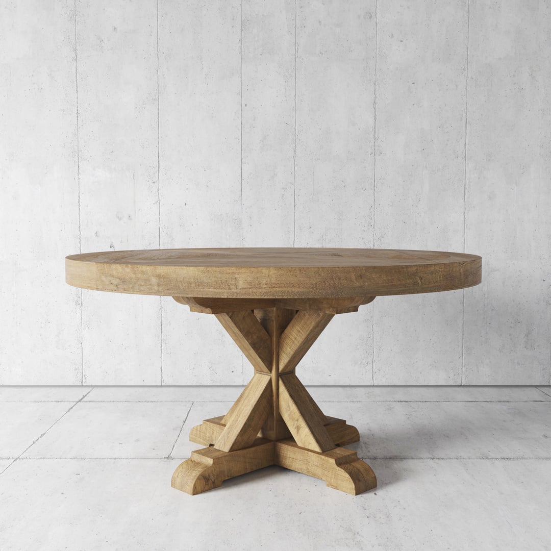 A round wooden table, a prime piece of furniture with a robust, crossed-leg base, is placed on a concrete floor against a plain, concrete wall background.