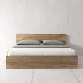 The Satillo Bed, featuring a wooden frame with a light brown finish, is adorned with neatly arranged gray pillows and a white bed sheet, set against a minimalist concrete wall background.