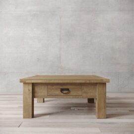 A Riverbend wooden coffee table with a single drawer is placed on a hardwood floor in front of a plain concrete wall.