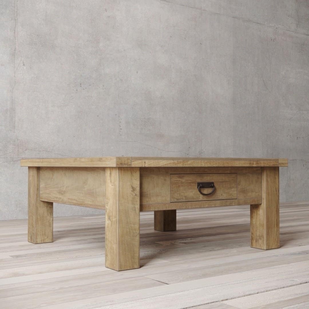 The Riverbend Coffee Table, featuring a single drawer and a metal handle, is set on a light wooden floor with a textured concrete wall in the background.