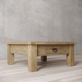 The Riverbend Coffee Table, featuring a single drawer and a metal handle, is set on a light wooden floor with a textured concrete wall in the background.