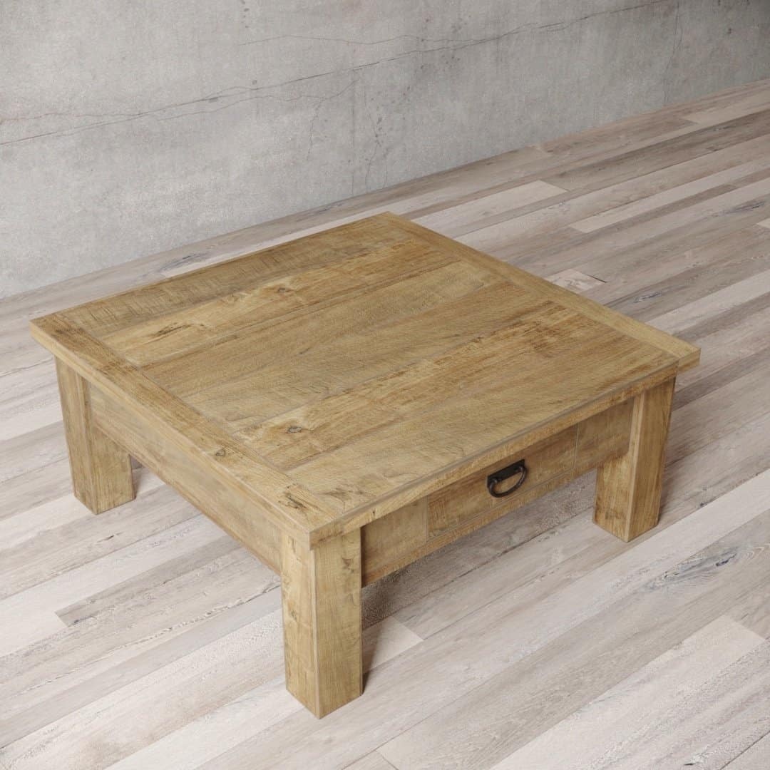 Urban Woodcraft 40 Riverbend Coffee Table - Natural (4) A Riverbend Coffee Table, square and wooden with a drawer, placed on a light-colored wooden floor against a plain concrete wall.