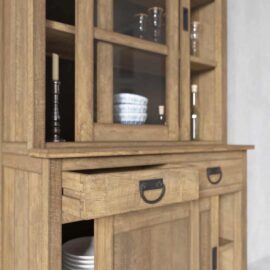 The Riverbend 36" Display Cabinet with glass doors showcases glassware and dishes. The slightly open drawer reveals additional plates inside, while candles and decorative pieces adorn the shelves.