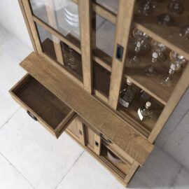 ***The Riverbend 36" Display Cabinet with glass doors and a partially open drawer. Inside are various glassware and bottles. The cabinet is placed against a light-colored wall.***