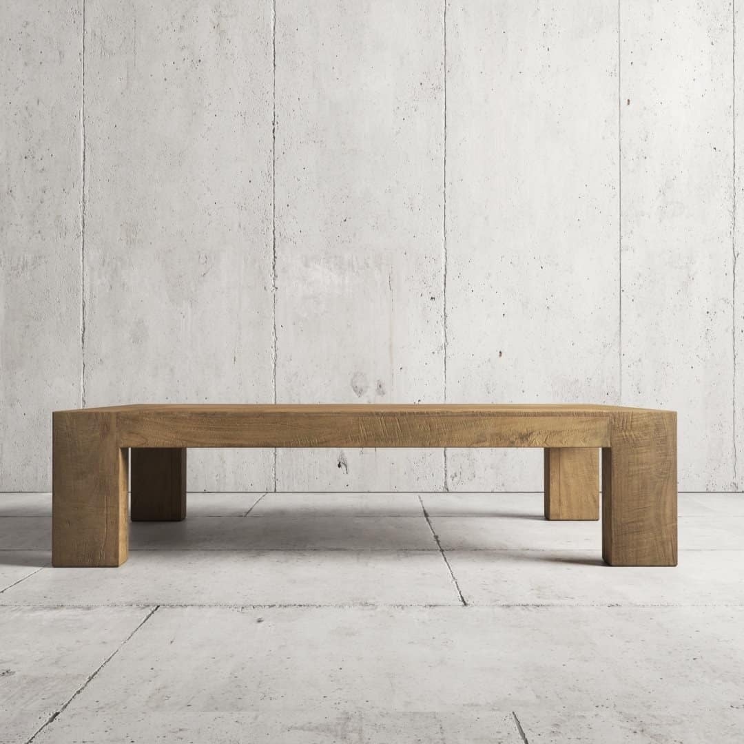The Madison Coffee Table, a low wooden centerpiece with a minimalist design, placed against a textured concrete wall and floor background.