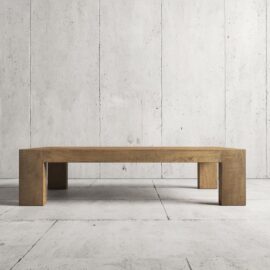 The Madison Coffee Table, a low wooden centerpiece with a minimalist design, placed against a textured concrete wall and floor background.