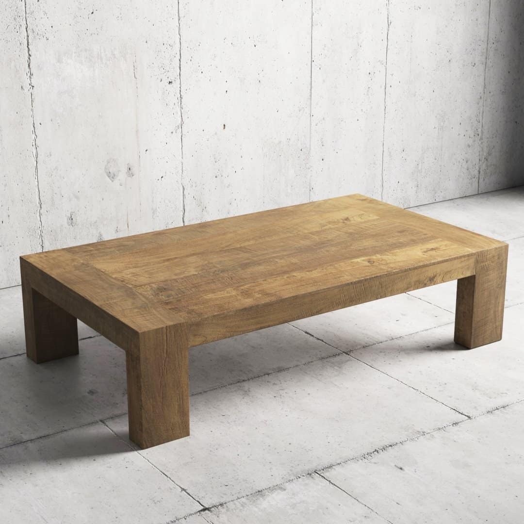 Urban Woodcraft 55 Madison Coffee Table - Natural (3) The Madison Coffee Table, a rectangular wooden piece with thick legs, is placed on a light gray concrete floor against a textured concrete wall.