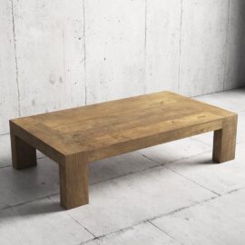 The Madison Coffee Table, a rectangular wooden piece with thick legs, is placed on a light gray concrete floor against a textured concrete wall.
