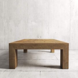 A Madison Coffee Table with thick wooden legs set against a plain concrete wall and floor.