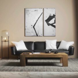 A modern living room with a black leather sofa, four white pillows, a Madison Coffee Table, two abstract black-and-white paintings on the wall, and a tall lamp with a glass shade.