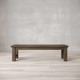 A straightforward, rectangular wooden Square Dining Bench with block legs stands on a light wooden floor against a plain, light grey concrete wall.