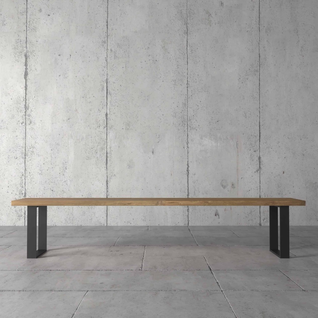 The Soma Dining Bench, featuring a minimalist wooden design with black metal legs, is placed against a bare concrete wall and concrete floor.