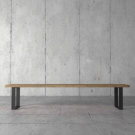 The Soma Dining Bench, featuring a minimalist wooden design with black metal legs, is placed against a bare concrete wall and concrete floor.