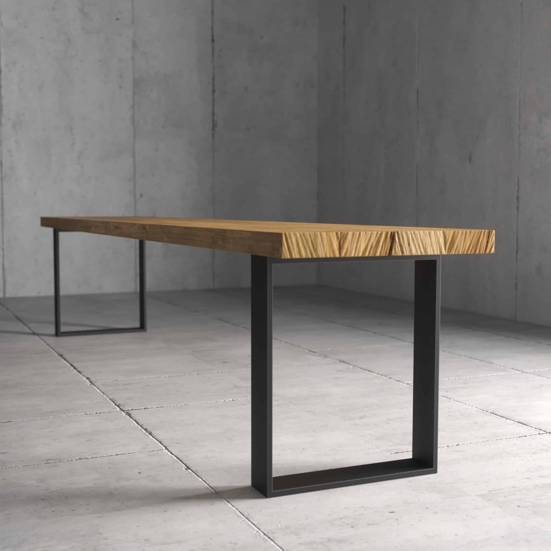 A minimalist Soma Dining Bench featuring a thick wooden slab top and black metal square legs, positioned in an austere, concrete-floored room.