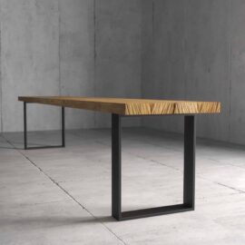 A minimalist Soma Dining Bench featuring a thick wooden slab top and black metal square legs, positioned in an austere, concrete-floored room.