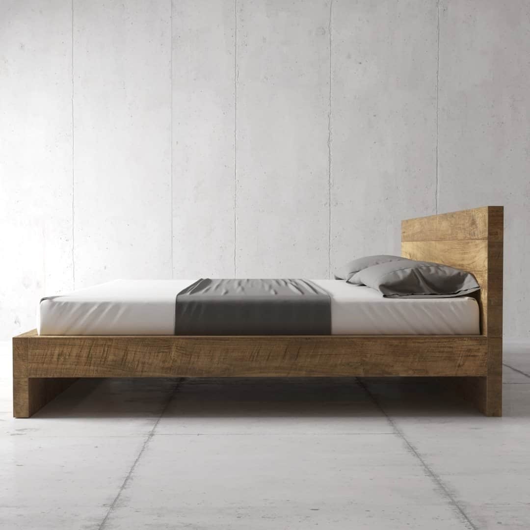 The Lugano Bed, featuring a minimalist wooden bed frame paired with a white mattress, complemented by a gray bed runner and pillows, stands against a plain, light-colored wall.