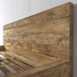 Close-up of the Lugano Bed frame with a rustic, weathered finish against a plain wall. The headboard and slats are visible.