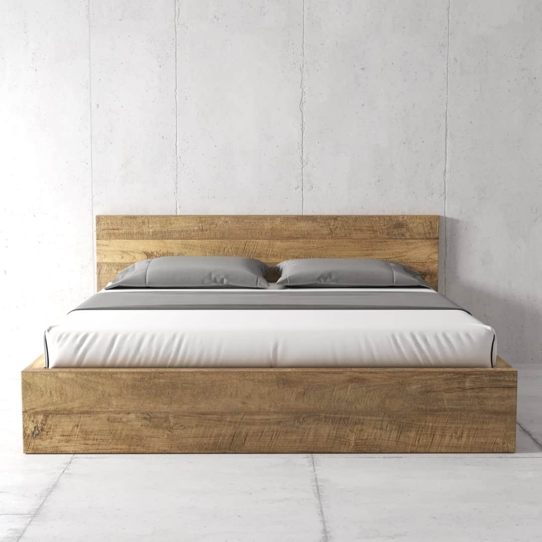 Urban Woodcraft Lugano Bed - Natural (5) The Lugano Bed, featuring a wooden frame and headboard, is a minimalist piece with a neatly made bedspread and two gray pillows set against a plain, concrete wall.